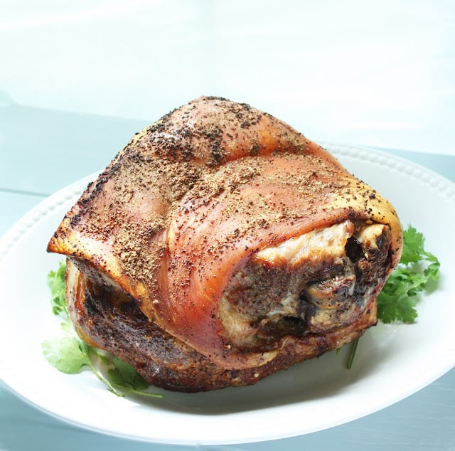 whole roasted pork shoulder with crispy skin on a white platter