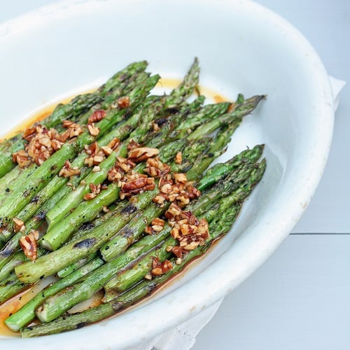 low carb grilled asparagus with sriracha and toasted pecans in a white oval dish