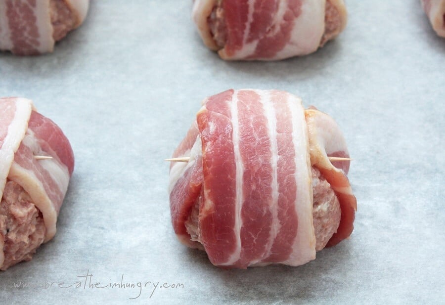 jalapeno popper meatballs shown raw on a cookie sheet lined with parchment paper before baking.