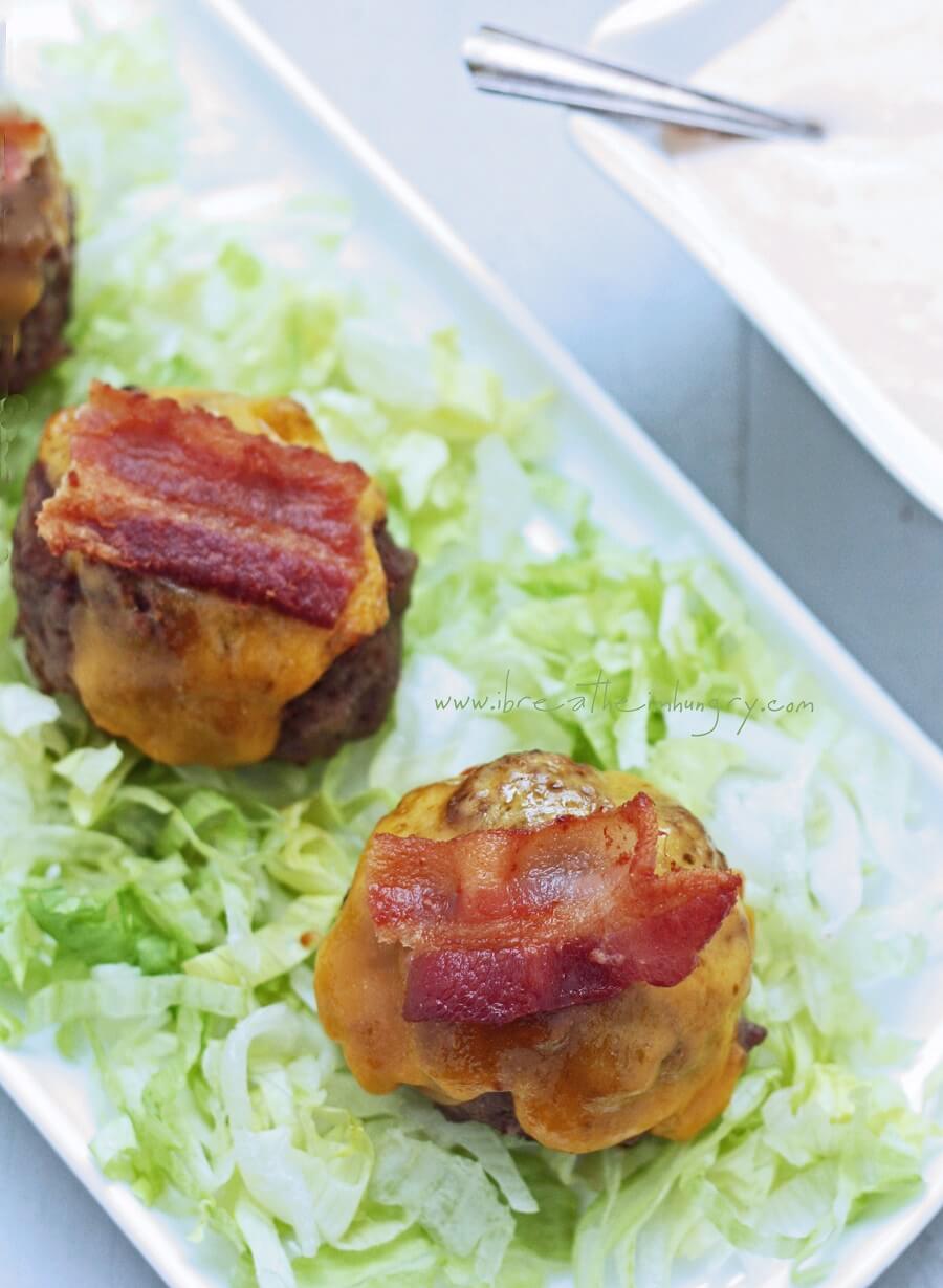 Top view of 3 keto bacon cheeseburger meatballs on a bed of lettuce with a bowl of special sauce in the upper right corner