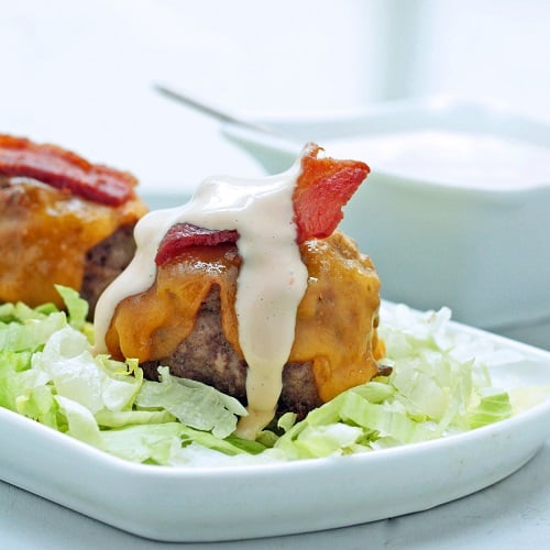 Keto Bacon Cheeseburger Meatballs on a white platter and a bed of iceberg lettuce with a drizzle of special sauce