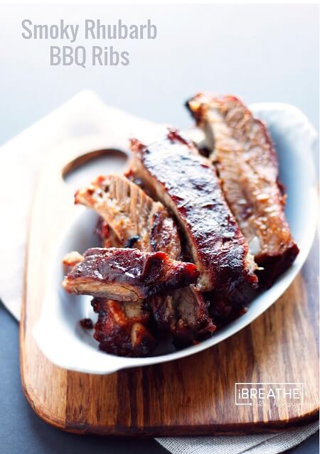 Smoky Rhubarb BBQ Ribs, cut into sections and placed in a white ramekin on a wooden cutting board