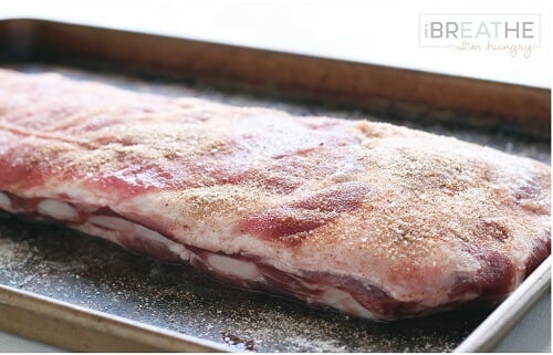 A rack of ribs on a baking sheet, covered in seasonings and ready to go into the oven