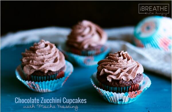 3 keto chocate zucchini cupcakes with mocha frosting on a teal serving board.
