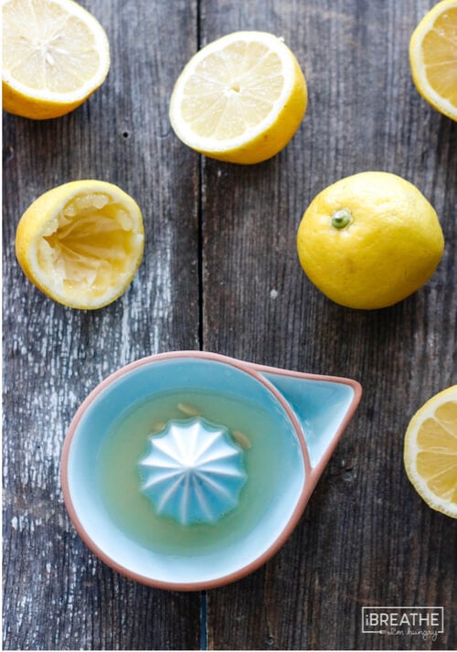 Process shot of lemons on a wooden cutting board, some cut in half and showing them juiced in preparation for the keto lemon pie