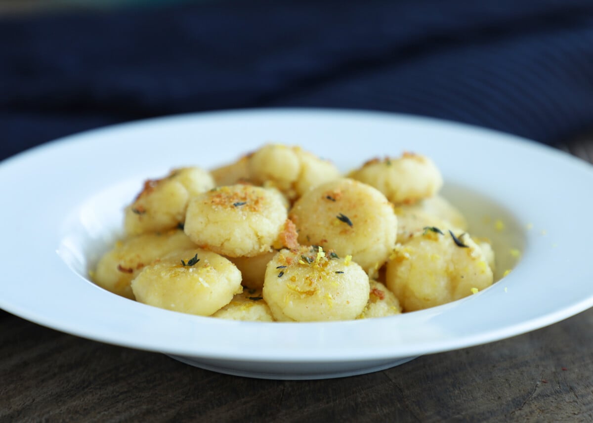Keto gnocchi in a white bowl garnished with lemon zest and fresh thyme leaves