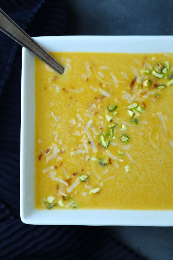 Top view of Keto Curried Squash Soup in square white bowl with pistachios and coconut