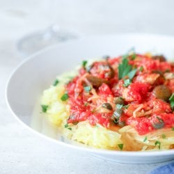 Keto Spaghetti Squash Puttanesca on a white plate with a blue napkin