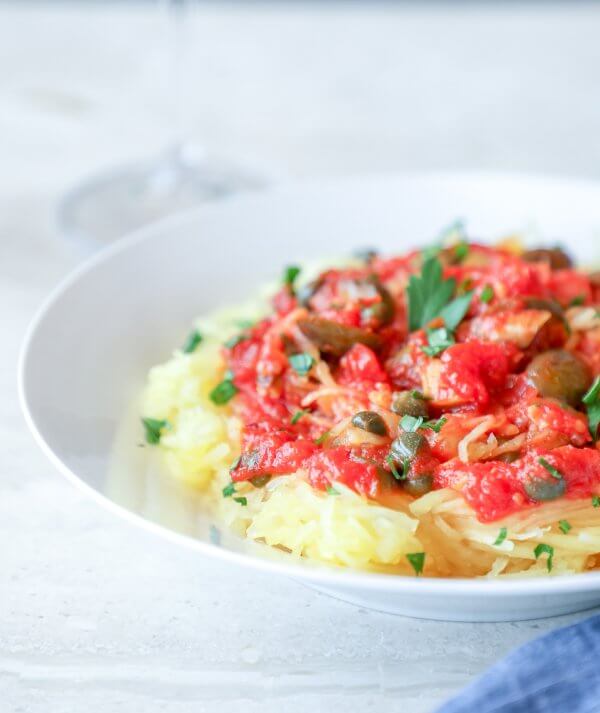 Keto Spaghetti Squash Puttanesca on a white plate with a blue napkin
