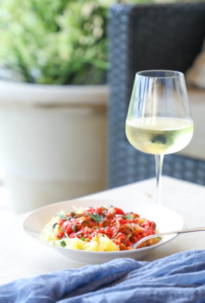 Keto Spaghetti Squash Puttanesca on a patio table with white wine