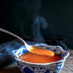 keto roasted tomato & garlic soup spoonful with steam against black background