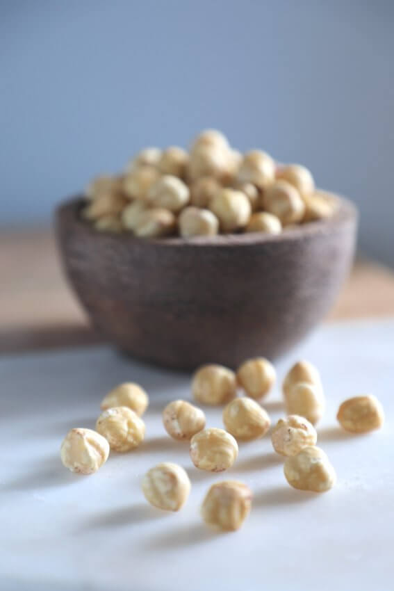 wooden bowl filled with shelled hazelnuts and scattered hazelnuts on marble board