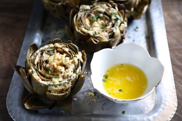 Flower shaped white bowl of melted butter with an artichoke