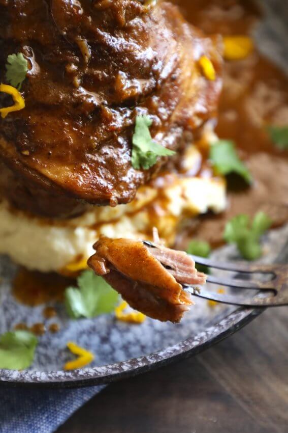 Forkful of Keto lamb shank meat with a blue enamelware plate in background