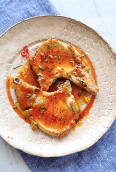 Two keto pork chops on a tan pottery plate with sweet chili sauce on top