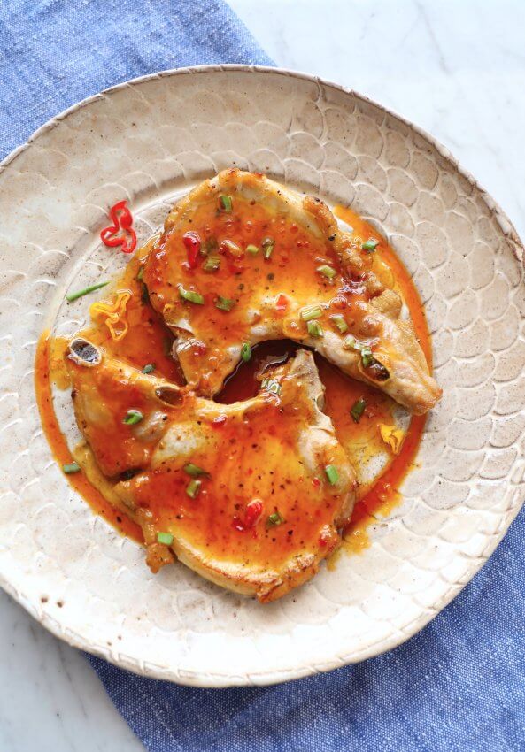 Two keto pork chops on a tan pottery plate with sweet chili sauce on top