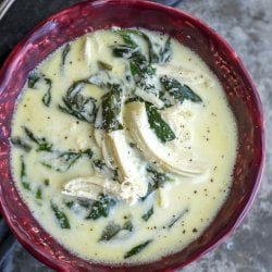 keto chicken Florentine soup in a magenta bowl with an antique spoon on a grey napkin in the background