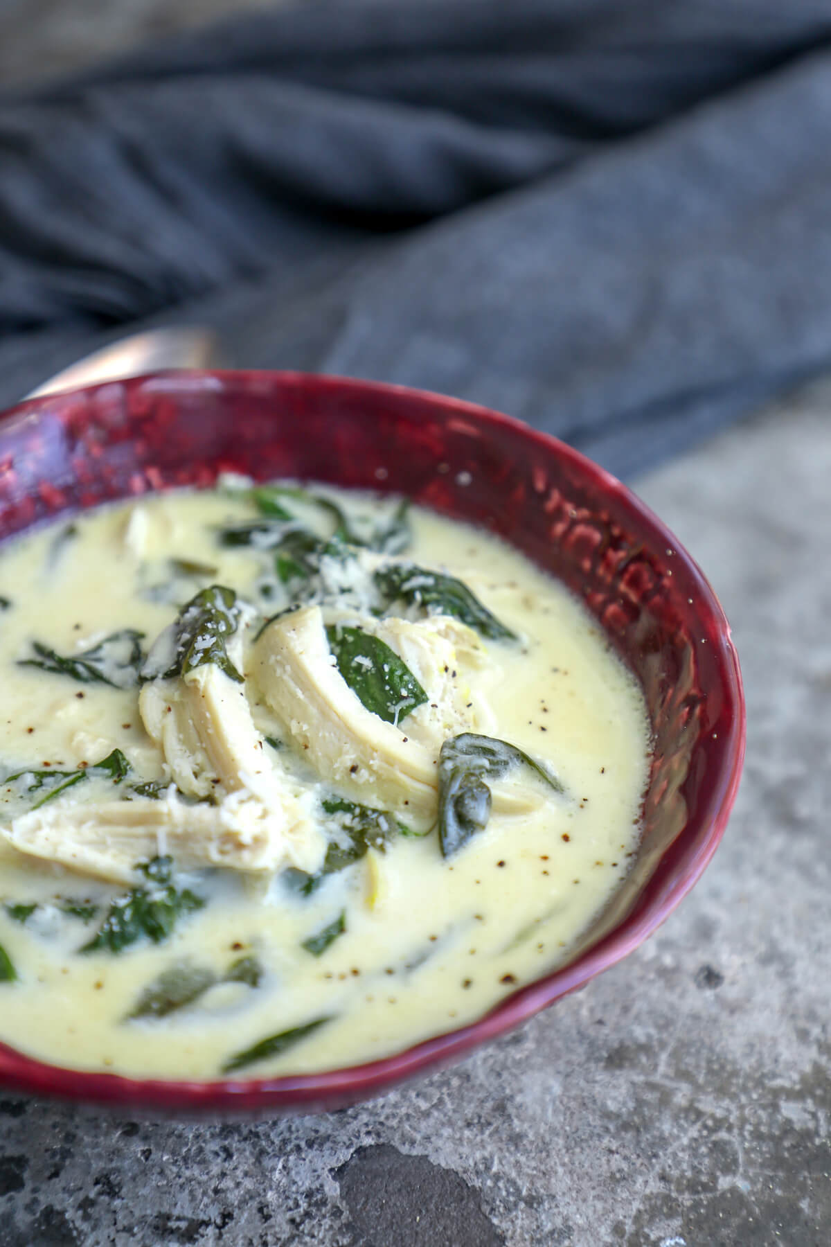 keto chicken Florentine soup on a grey concrete background with a grey napkin