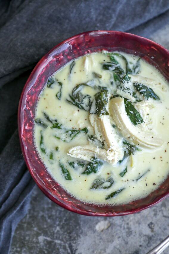 keto chicken Florentine soup in a red bowl on a grey concrete background with a grey napkin shot from above with chunks of chicken on top