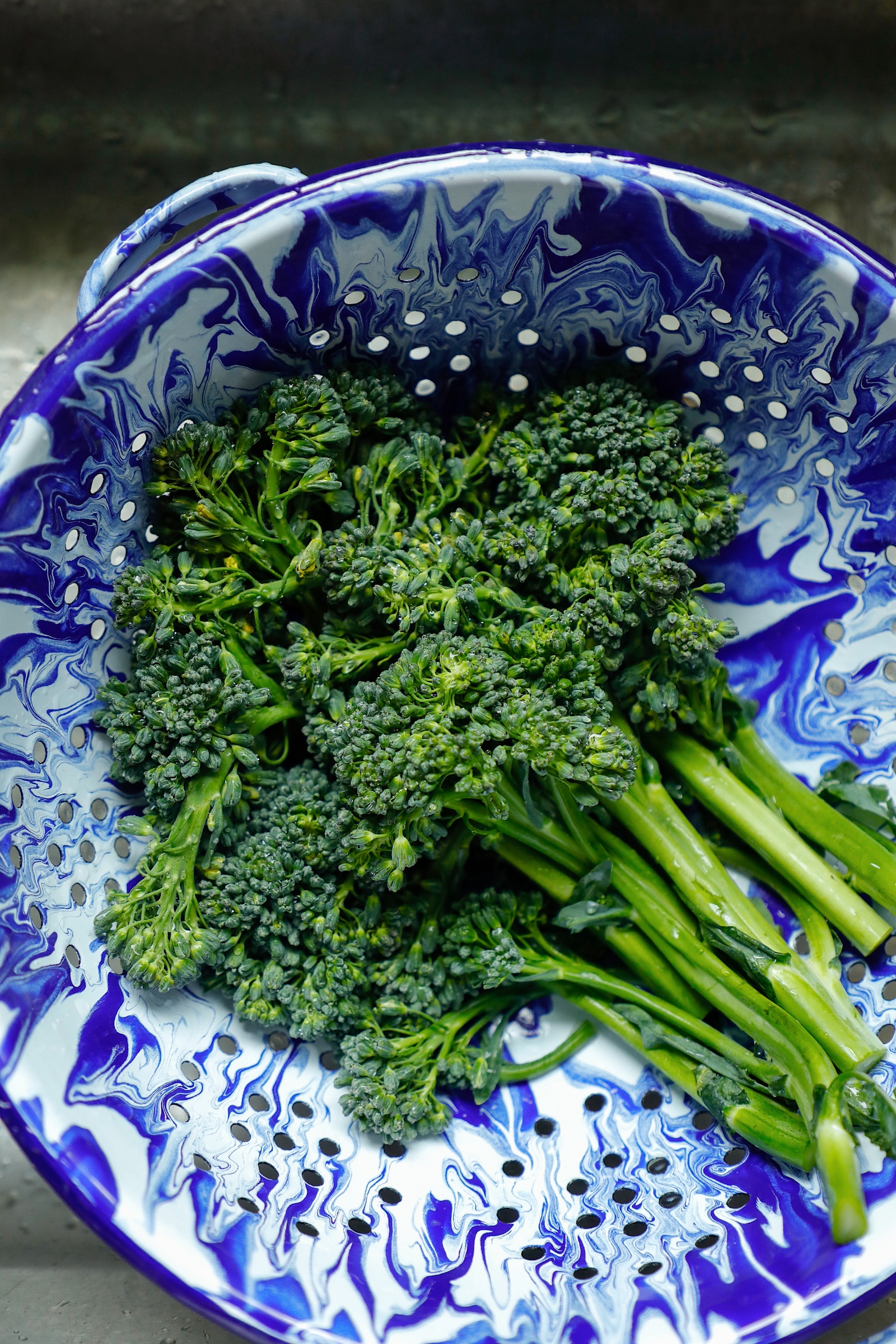 raw broccolini in a blue and white colander