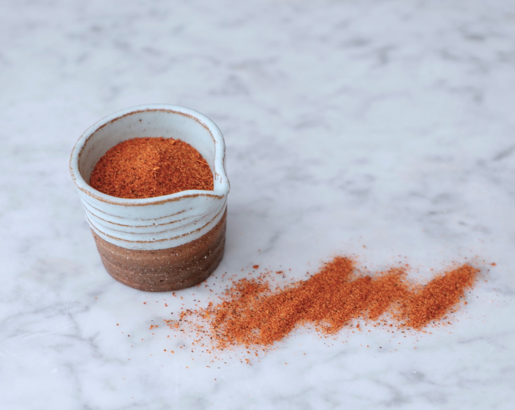 Homemade cajun seasoning sprinkled on a marble board from a pottery bowl