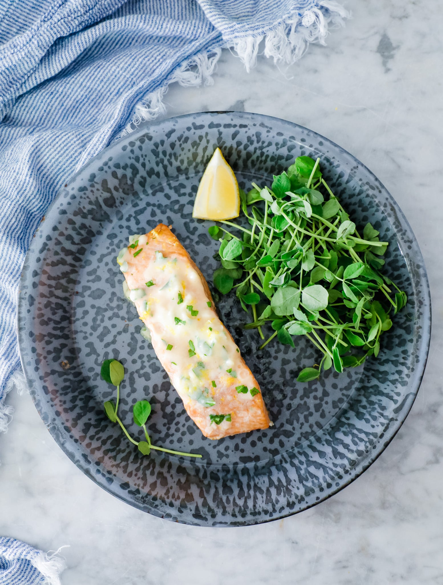 salmon fillet with Maitre de Butter on top served on a blue plate with green salad and lemon garnish