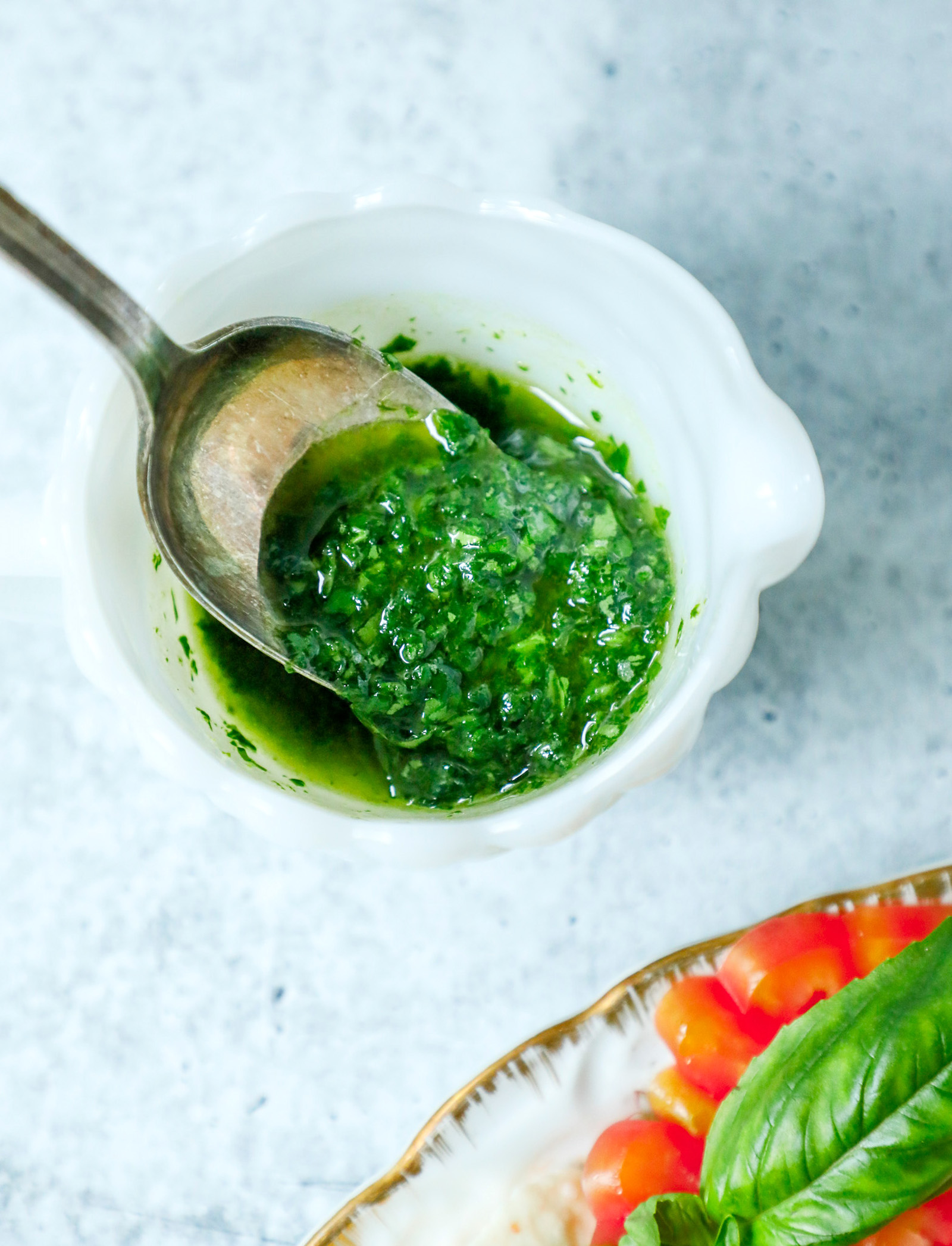 A white dish full of basil oil with a spoon inside.