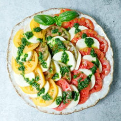 Top view of a caprese salad using green, yellow and red tomatoes on a round platter.