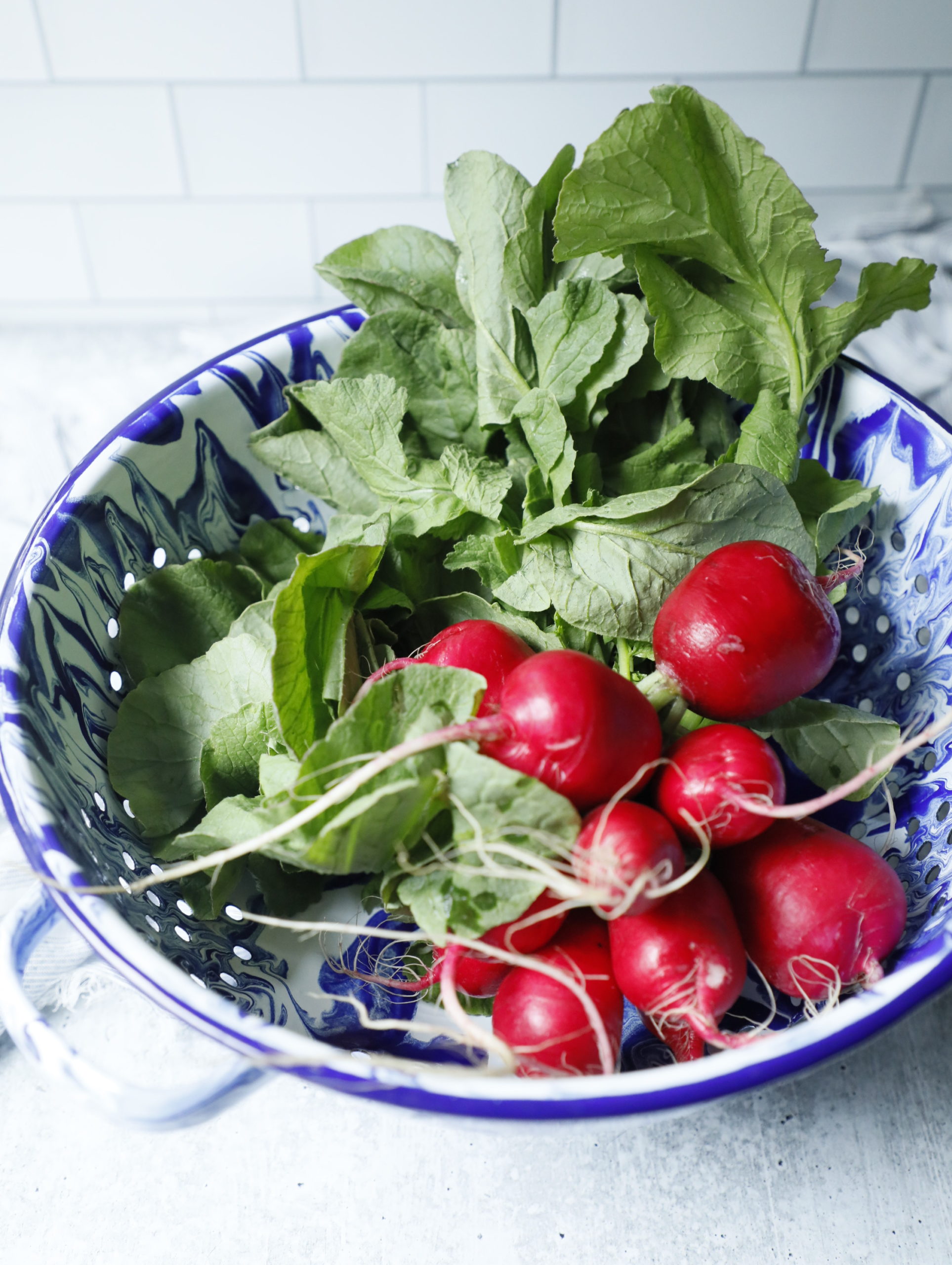 radishes with their tops on in a blue and white colander after washing.