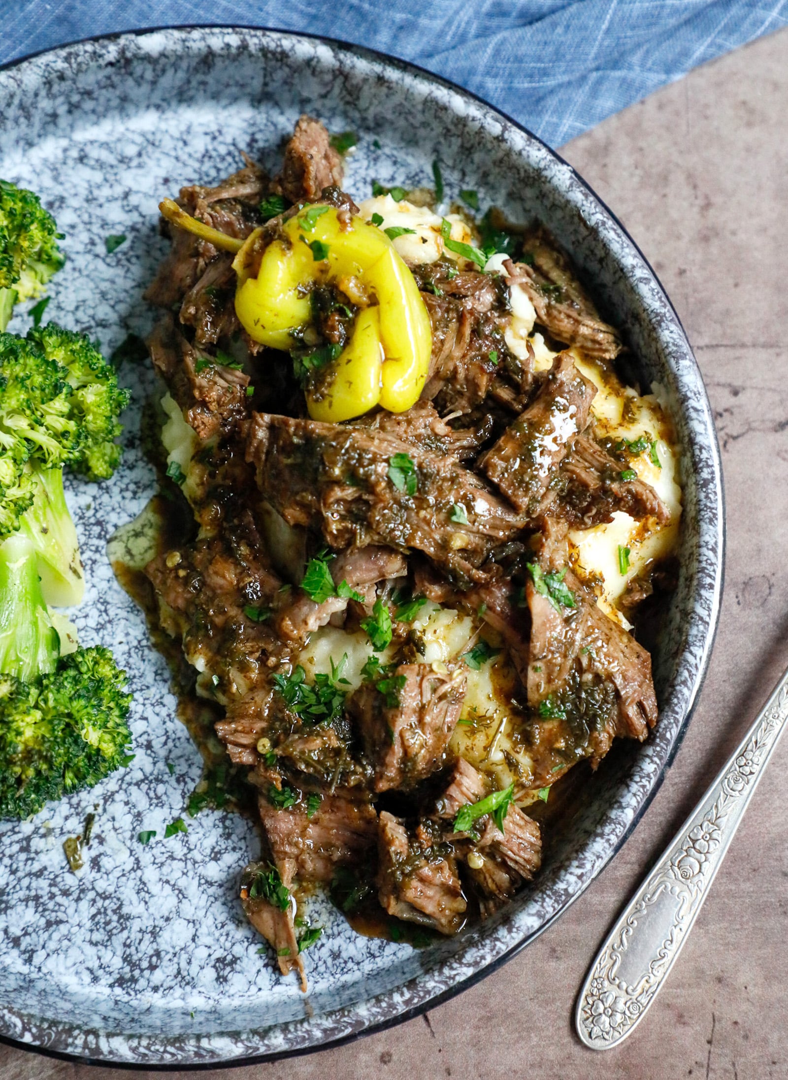Plateful of Keto Mississippi Pot Roast with a side of roasted broccoli and a pepperoncini on top for garnish.