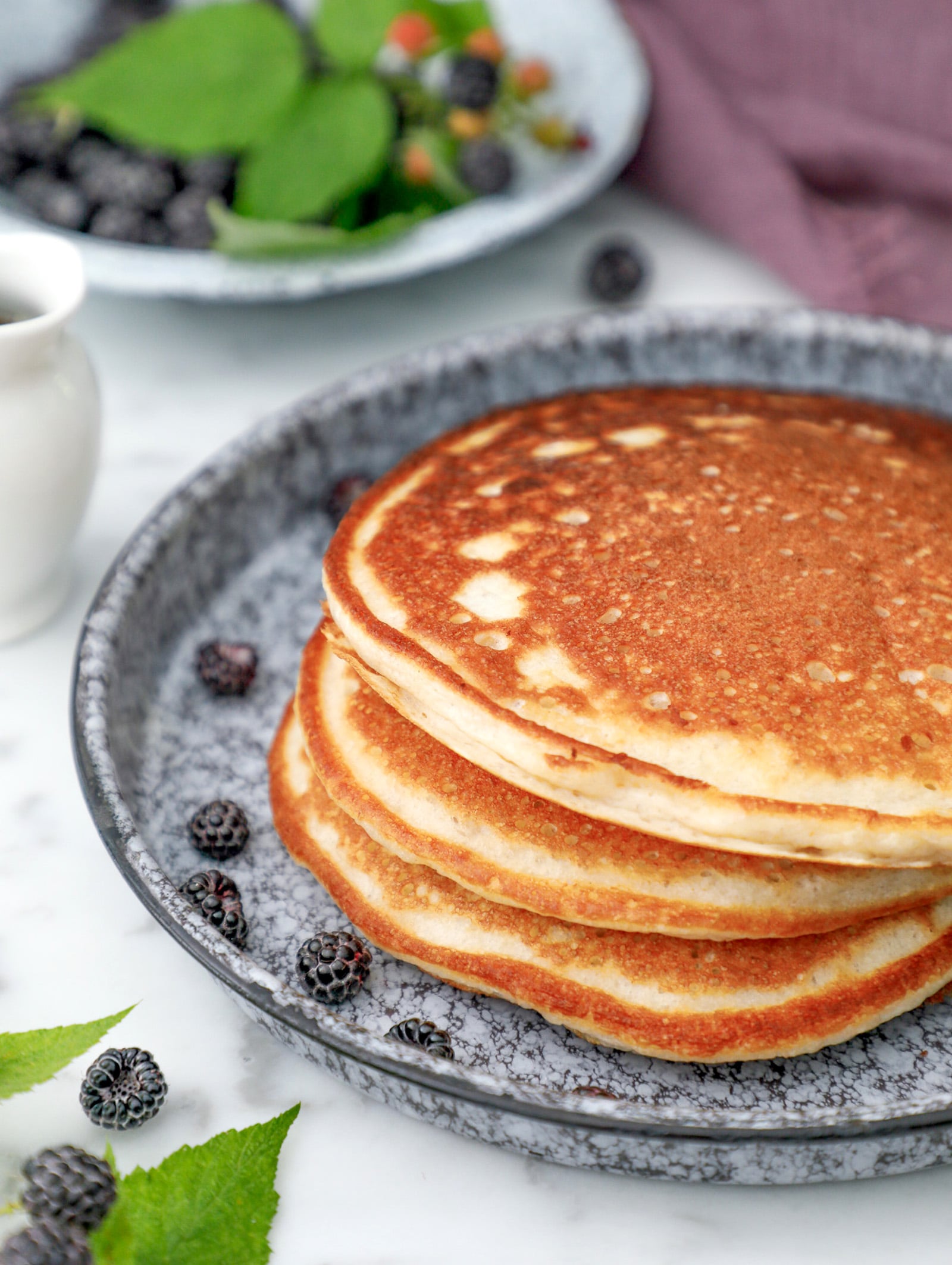 Stack of high protein pancakes on a blue plate with black raspberries for garnish