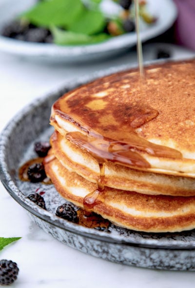 A stack of three high protein pancakes with maple syrup running down the side.
