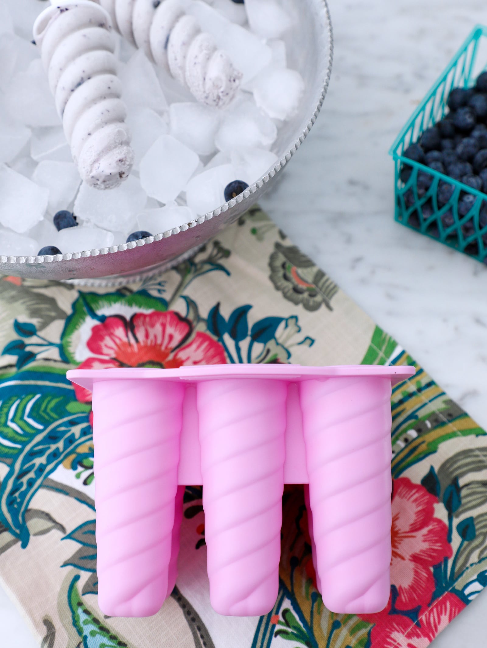 blueberry protein popsicles I the background with the pink silicone mold used to make them showing in the foreground