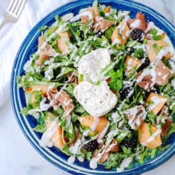 Arugula and Burrata salad with prosciutto, cantaloupe and blackberries on a blue pottery plate
