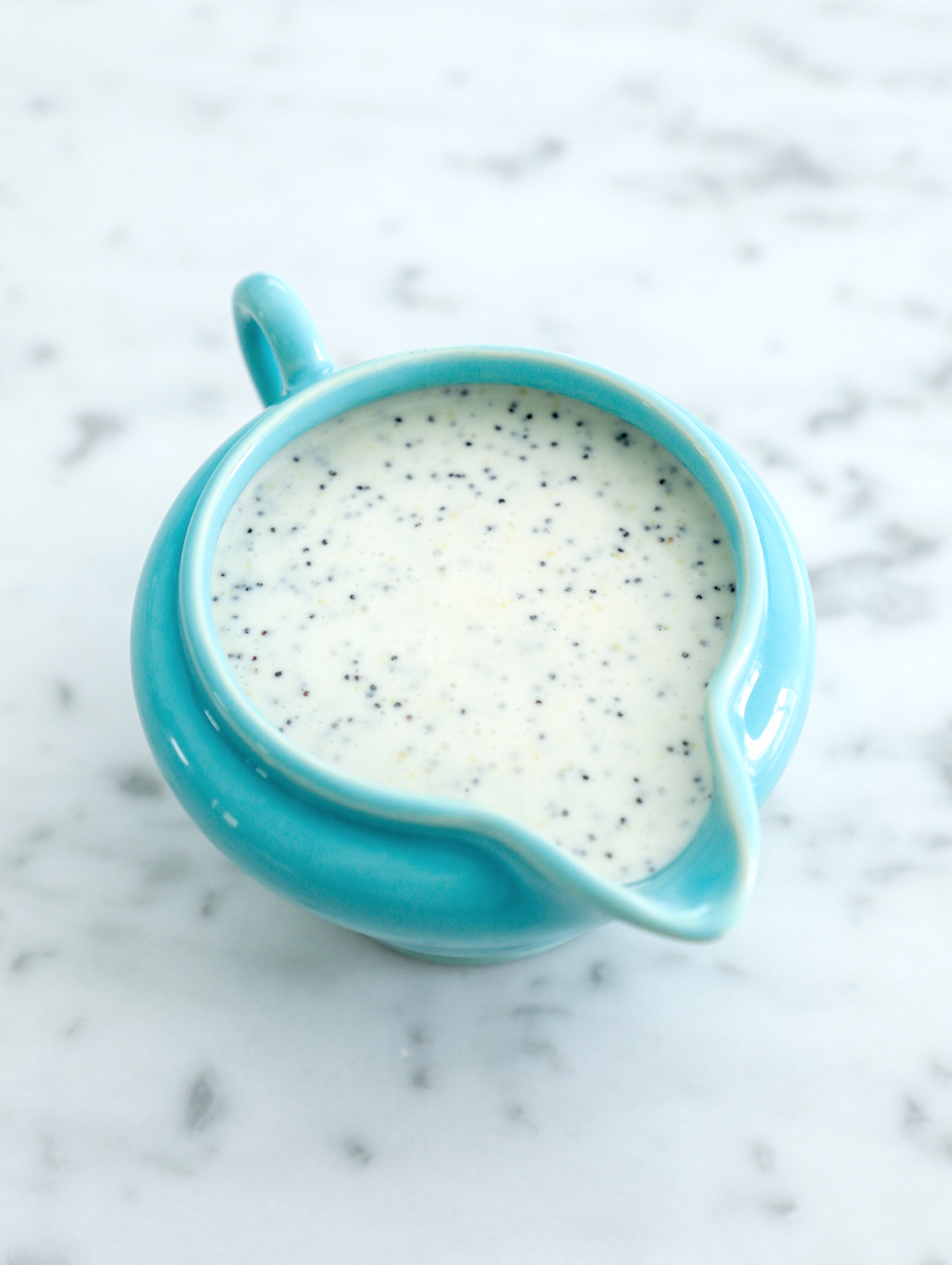 lemon poppy seed dressing in a turquoise blue pitcher on a marble background