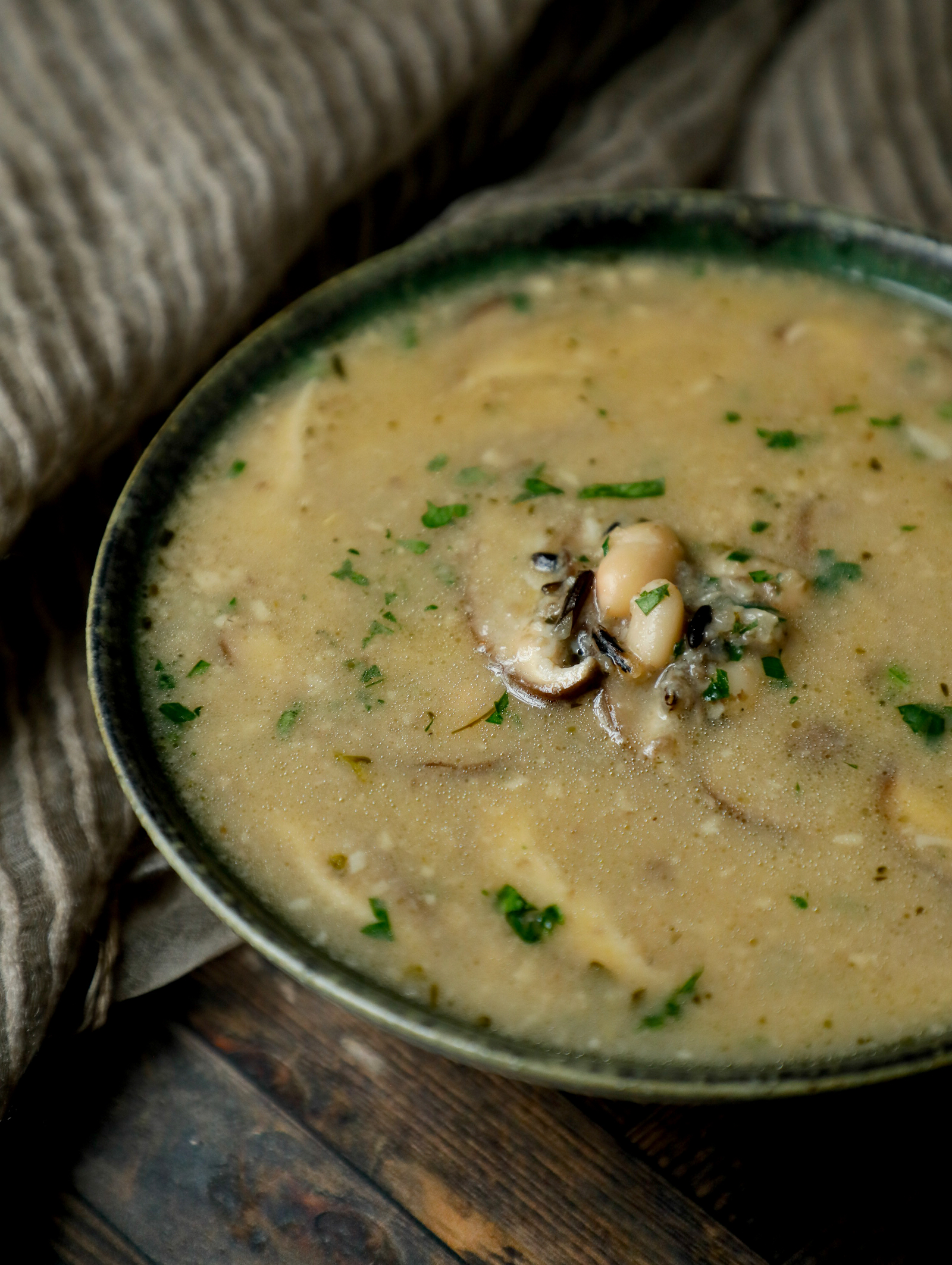 Side view of high protein mushroom and wild rice soup in a green pottery bowl on a wooden background