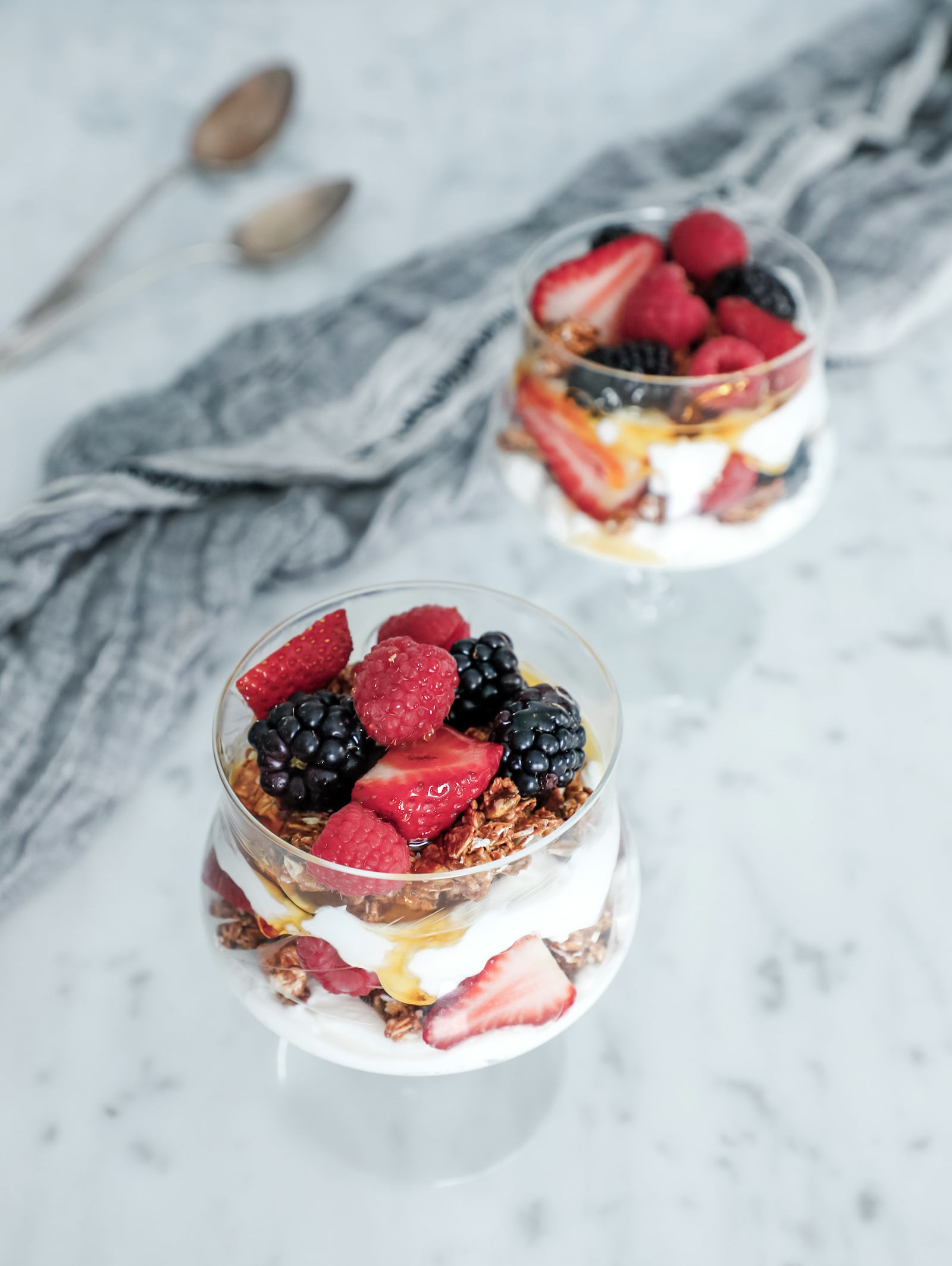 Top view of high protein yogurt and granola parfaits with mixed berries and honey in crystal goblets.