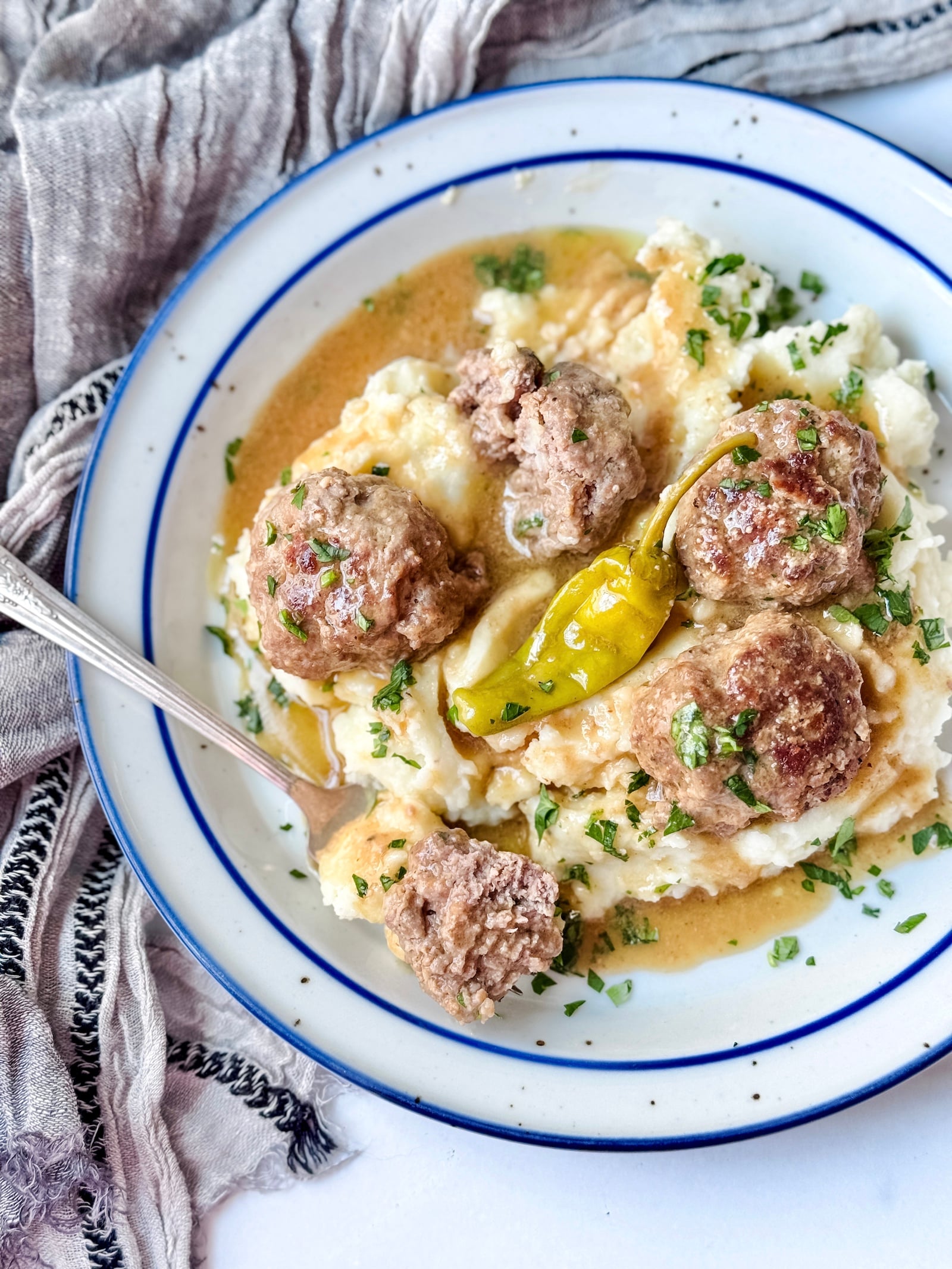 Top view of Mississippi pot roast meatballs with half of a meatball on a fork showing the texture, with mashed potatoes