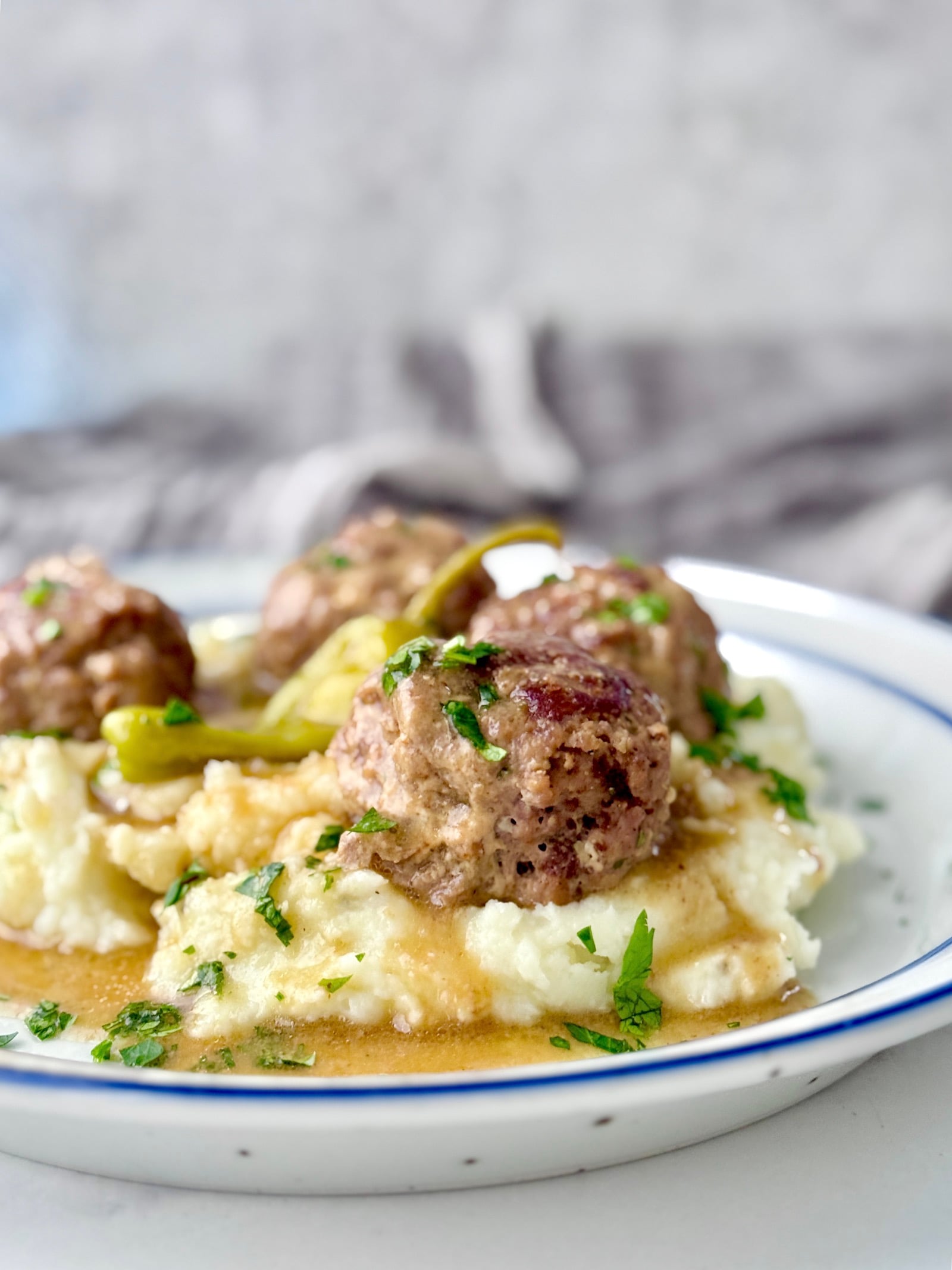 Mississippi Meatballs on a bed of mashed potatoes and swimming in gravy garnished with chopped parsley