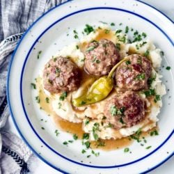 Mississippi Pot Roast Meatballs on a bed of mashed potatoes on a white pottery plate with blue trim