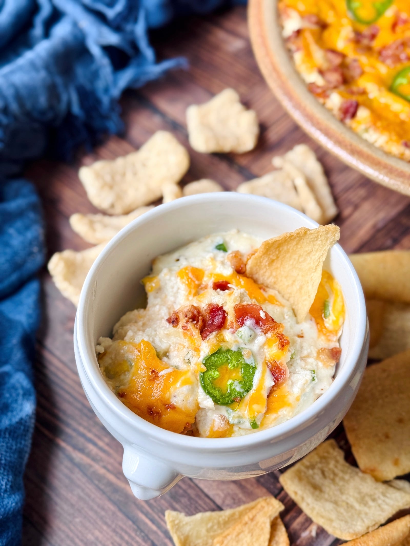 high protein jalapeno popper dip in a white bowl with pita chips and pork rinds scattered around it.