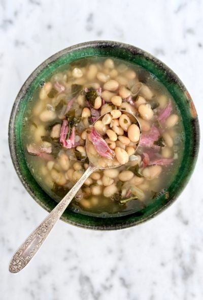 Smoky White Bean Soup in a green pottery bowl with an antique silver soup spoon