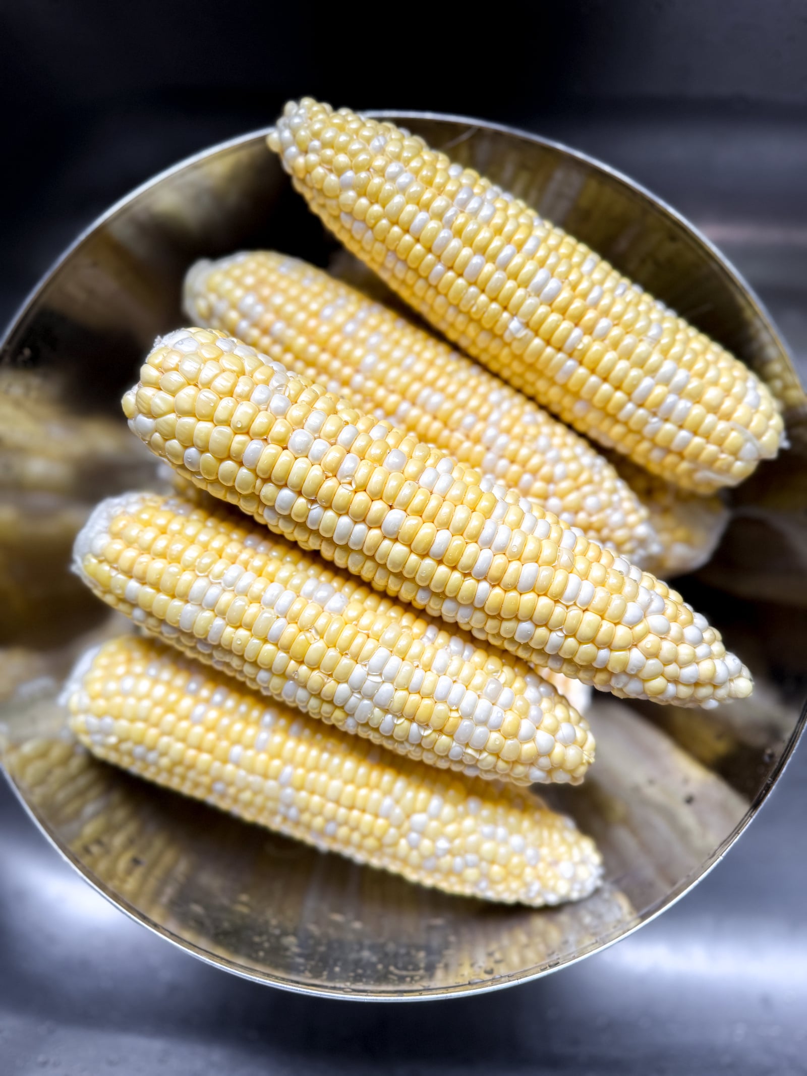 Ears of raw, shucked, corn in a stainless steel bowl