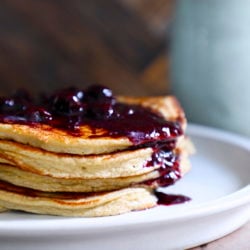 Fluffy Keto Pancakes with a berry compote on top and drizzling over the front of the stack.