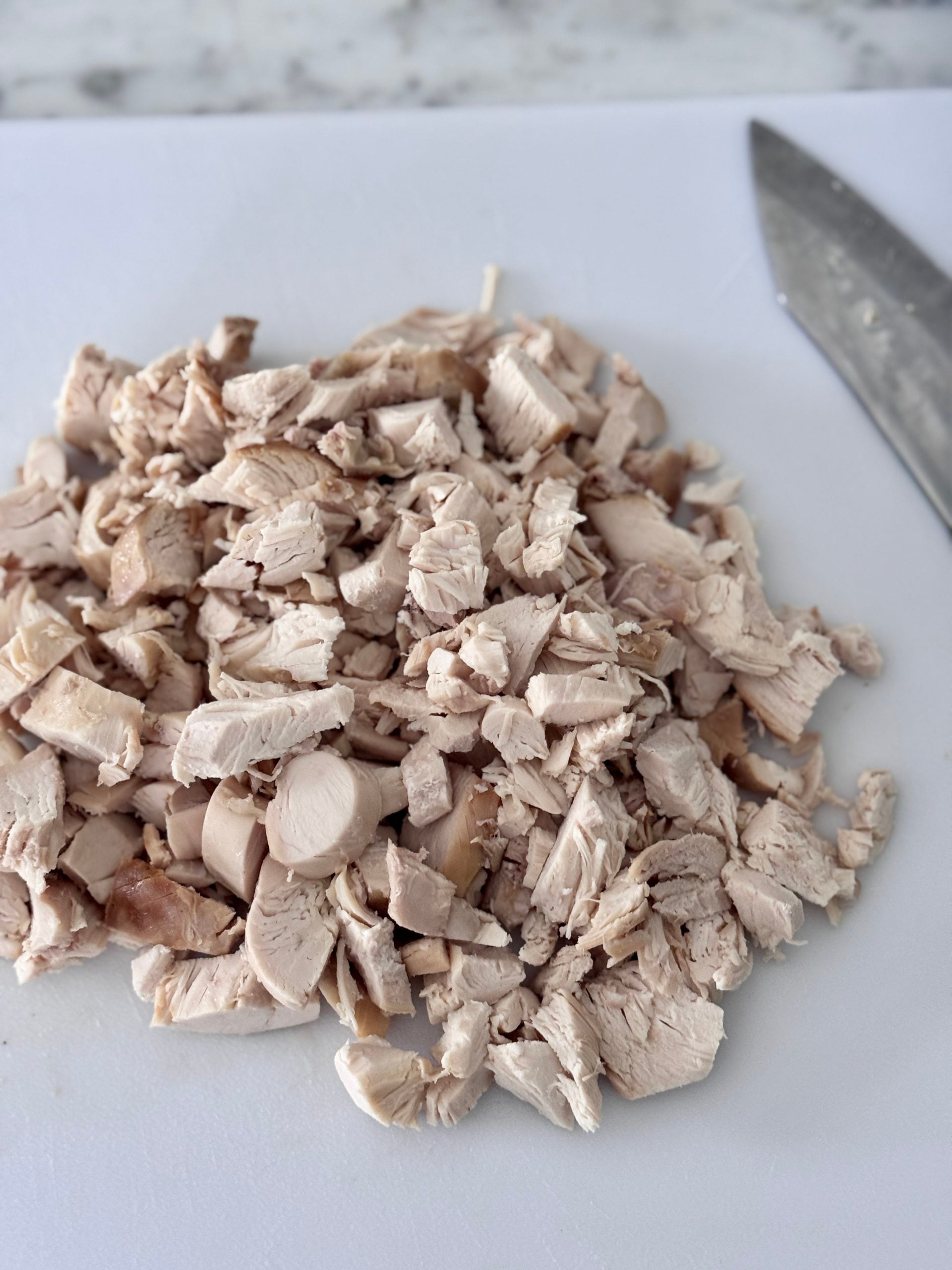 Chopped chicken breast from a rotisserie chicken on a white cutting board with a global brand chef's knife in the background