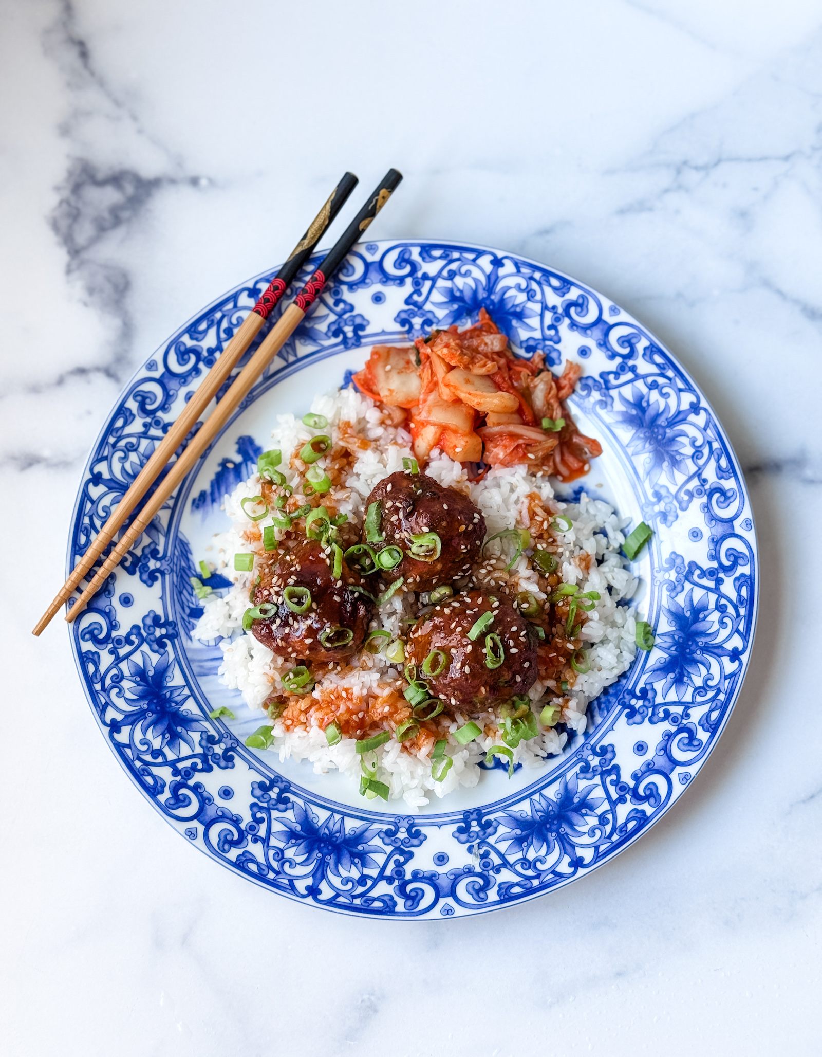 Korean beef meatballs served over white rice with kimchi and chopsticks on the blue and white plate