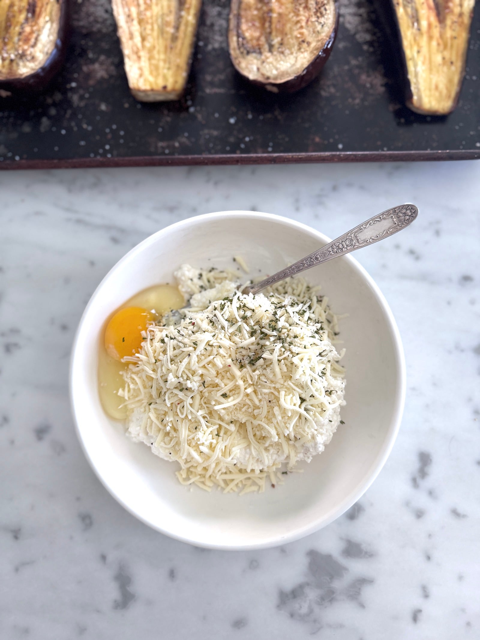 a white bowl filled with cottage cheese, egg, mozzarella cheese and seasonings for the high protein stuffed eggplant filling