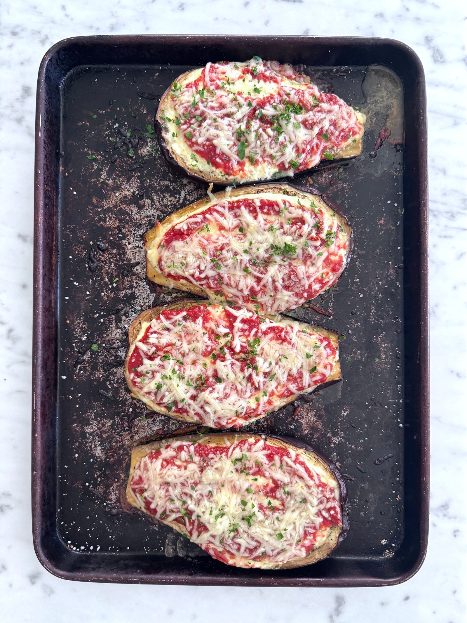 4 high protein low carb stuffed eggplant parmesan boats on a sheet pan after cooking